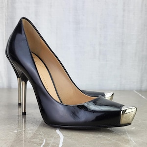 Könnte beinhalten: Schwarze Lackpumps mit spitzer Zehenpartie und silberner Metallkappe. Die Absätze sind im Stiletto-Stil und die Schuhe sind mit "Giuseppe Zanotti" gekennzeichnet.