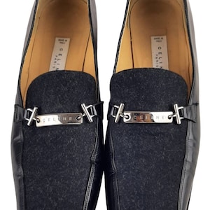 May include: Black leather loafers with a black wool panel and a silver metal buckle with the word "CELINE" engraved on it. The shoes are made in Italy and say "CELINE PARIS" on the inside.