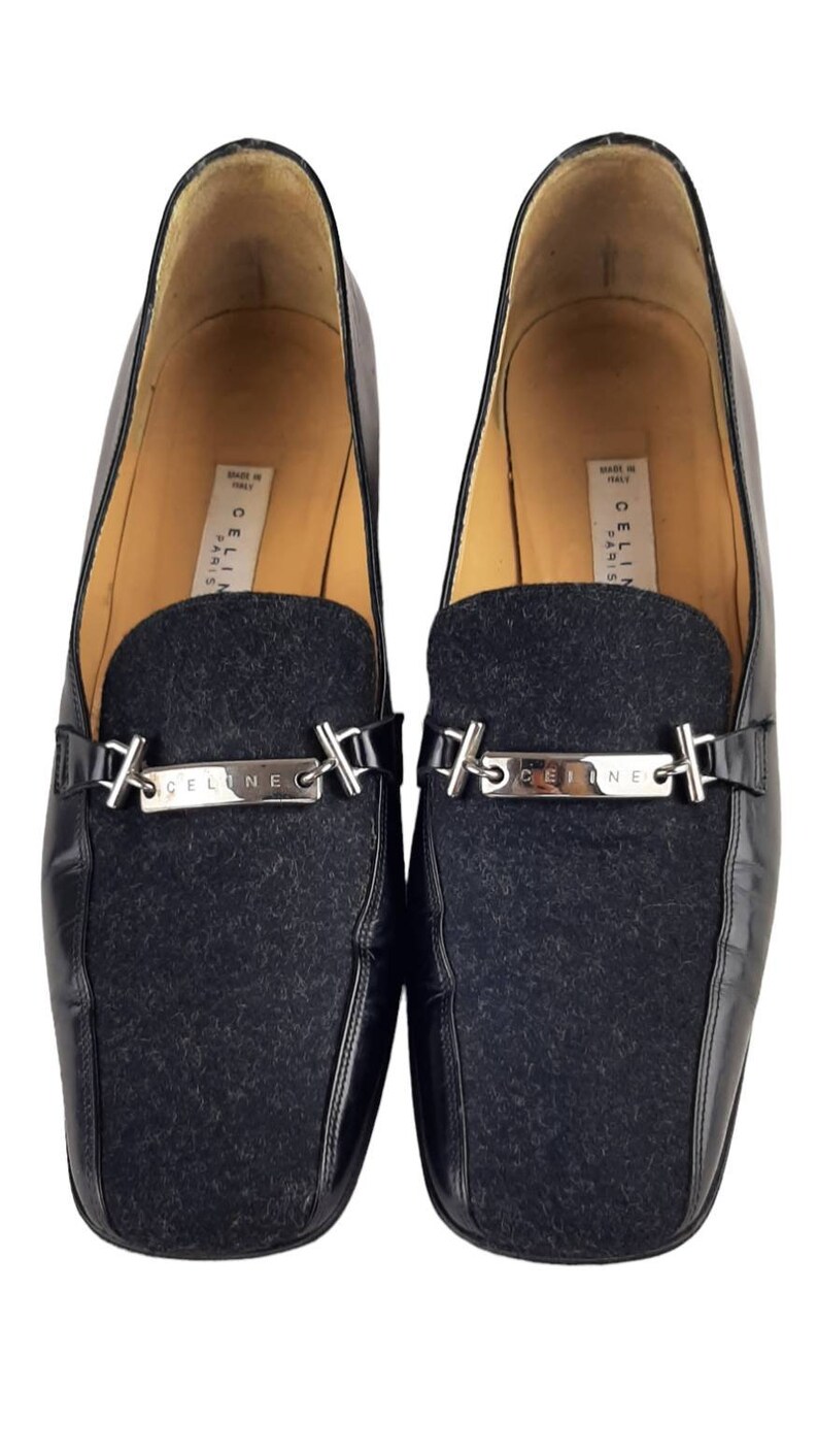 May include: Black leather loafers with a black wool panel and a silver metal buckle with the word "CELINE" engraved on it. The shoes are made in Italy and say "CELINE PARIS" on the inside.