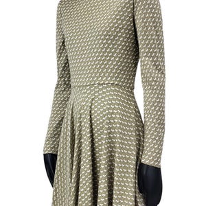 May include: A long-sleeved dress with a high neckline and a flared skirt. The dress is olive green with a repeating white pattern. The dress is displayed on a mannequin.