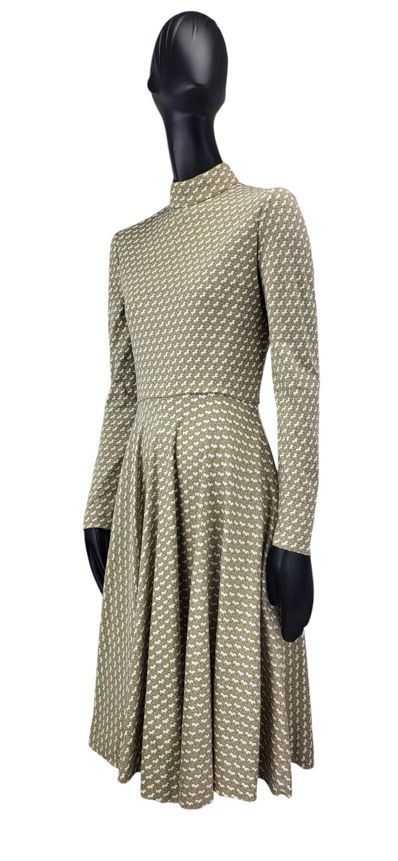 May include: A long-sleeved dress with a high neckline and a flared skirt. The dress is olive green with a repeating white pattern. The dress is displayed on a mannequin.
