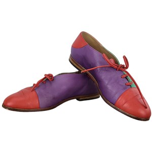 以下が含まれることがあります： 緑色のアクセントが付いた、紫と赤の革製のレースアップシューズのペアです。