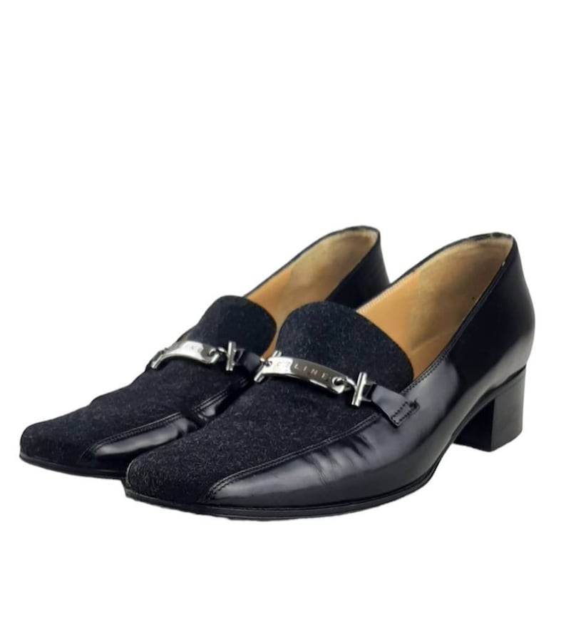 May include: Black leather and suede loafers with a silver buckle and the word "CELINE" engraved on it. The shoes have a low block heel.