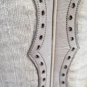 May include: Close-up of a pair of white leather boots with decorative stitching and a scalloped design.