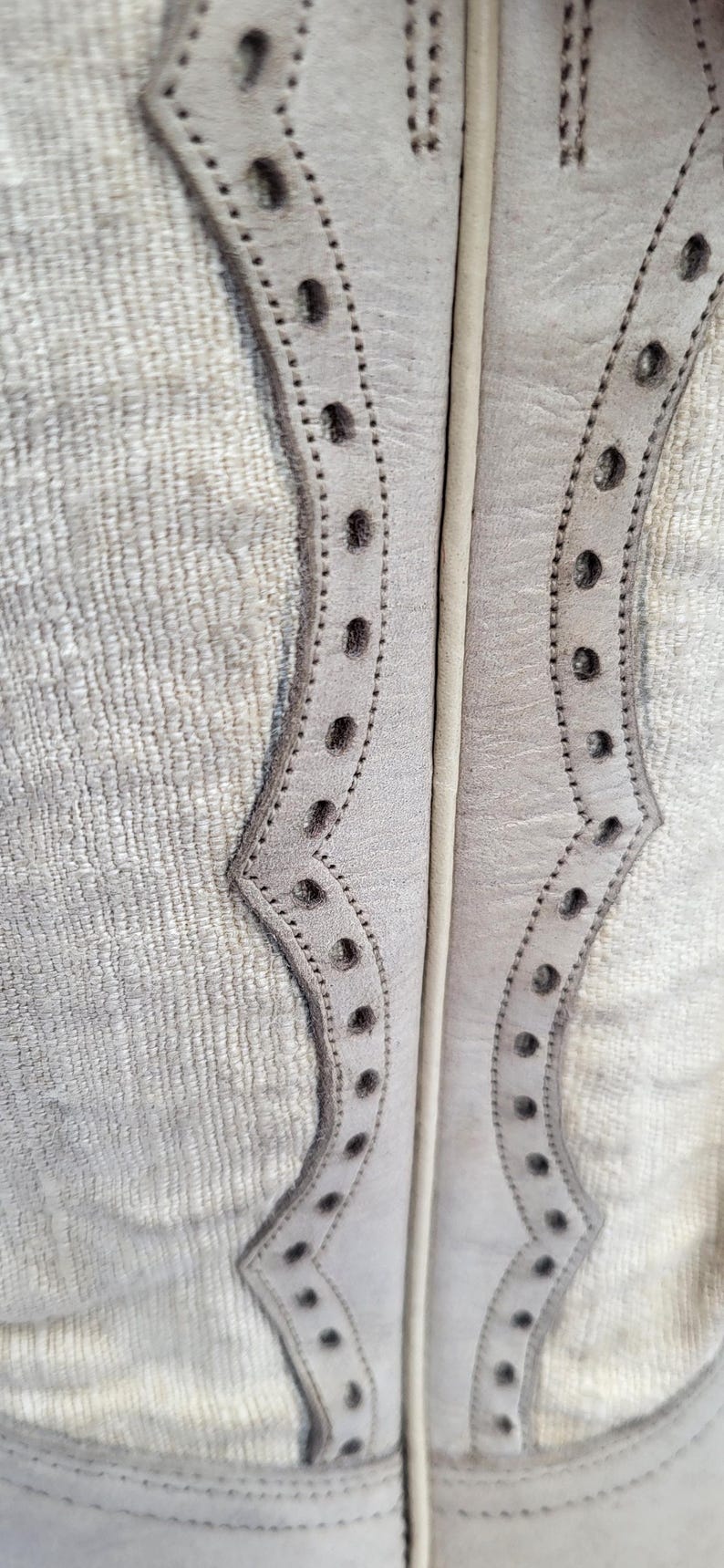 May include: Close-up of a pair of white leather boots with decorative stitching and a scalloped design.