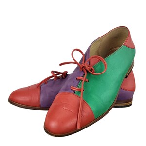 以下が含まれることがあります： 赤、緑、紫のパネルが付いた、マルチカラーの革靴のペア。靴には靴ひもがあり、丸みを帯びたつま先です。