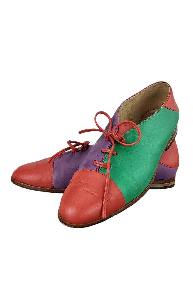 以下が含まれることがあります： 赤、緑、紫のパネルが付いた、マルチカラーの革靴のペア。靴には靴ひもがあり、丸みを帯びたつま先です。