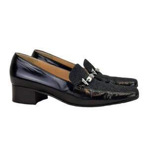 May include: Black leather heeled loafers with a silver buckle detail and a black and grey patterned fabric toe.