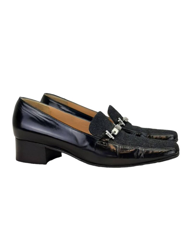May include: Black leather heeled loafers with a silver buckle detail and a black and grey patterned fabric toe.