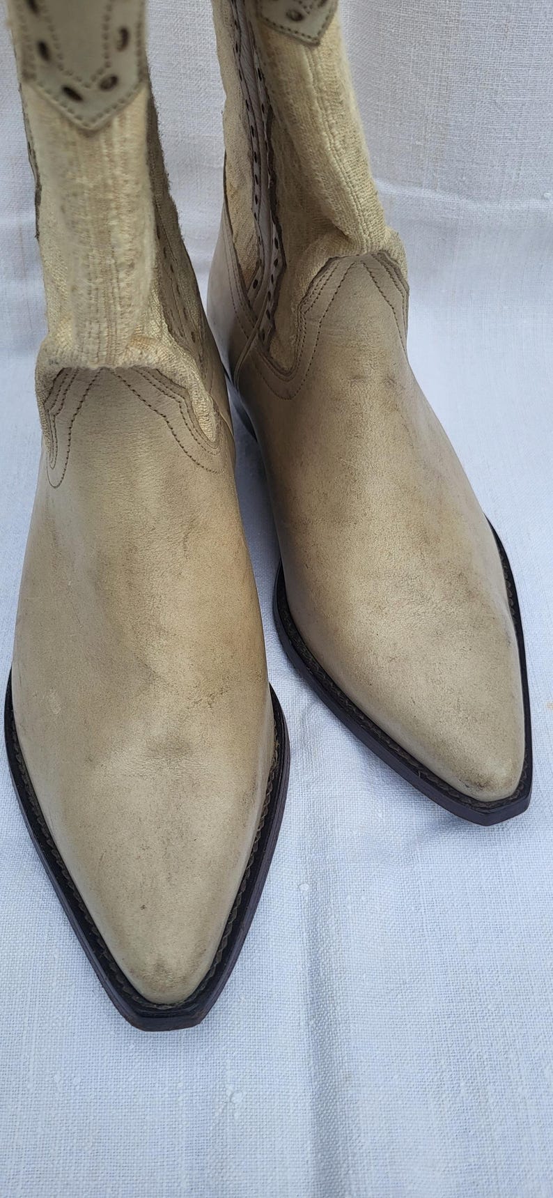 May include: A pair of light brown leather cowboy boots with pointed toes and a decorative stitching detail around the top of the boot.