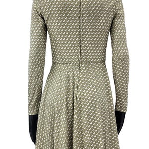May include: A long-sleeved dress in a light olive green color, featuring a repeating white pattern. The dress has a fitted bodice and a flared skirt, with a zipper running down the back. The dress is displayed on a mannequin.