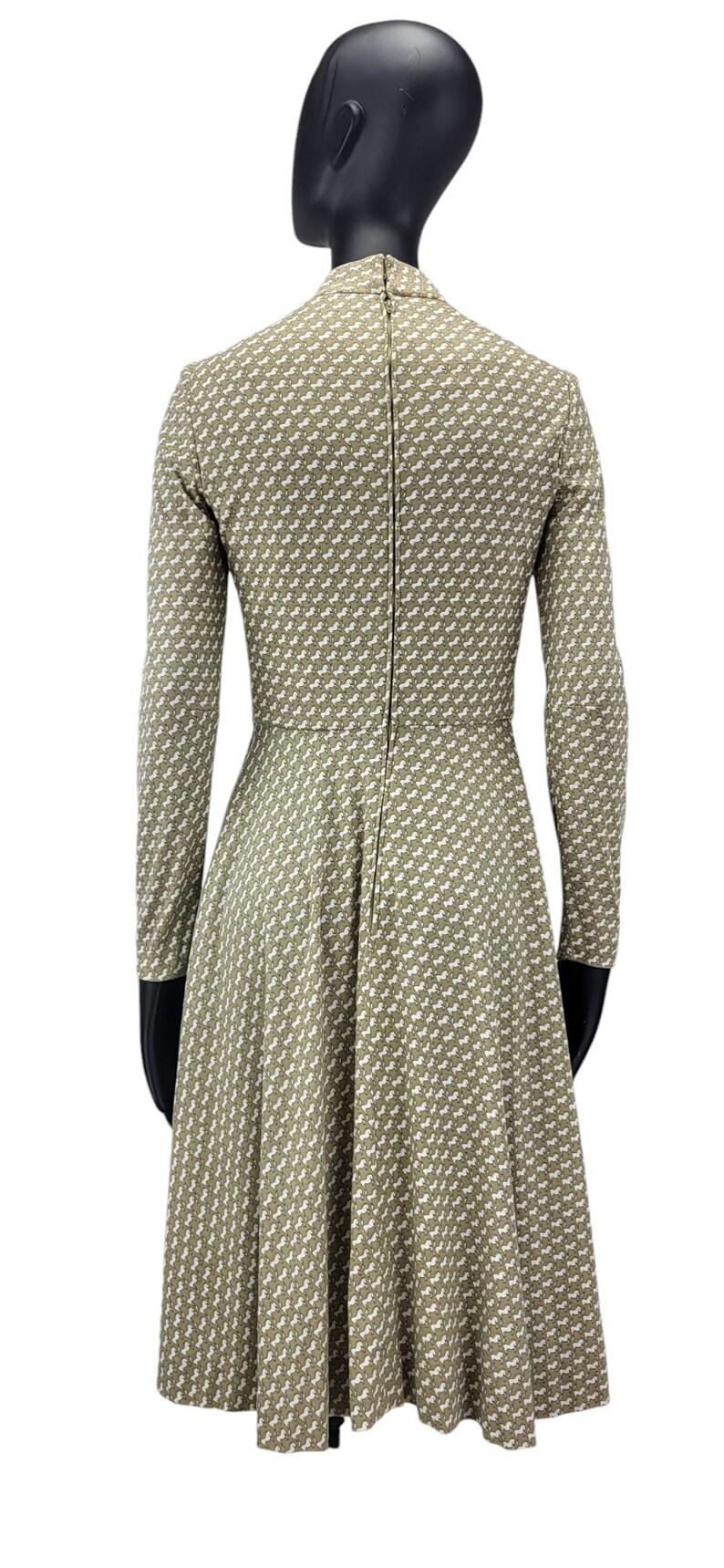 May include: A long-sleeved dress in a light olive green color, featuring a repeating white pattern. The dress has a fitted bodice and a flared skirt, with a zipper running down the back. The dress is displayed on a mannequin.