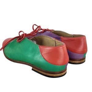 以下が含まれることがあります： 緑、赤、紫の革製のレースアップシューズのペア。シューズは丸みを帯びたつま先と低いヒールを持っています。