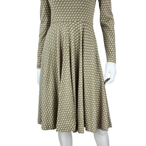 May include: A long-sleeved dress with a high neckline, featuring a repeating white and olive green pattern. The dress has a fitted bodice and a flared skirt, displayed on a mannequin. The mannequin is wearing beige heels.
