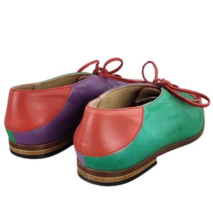 以下が含まれることがあります： 赤、紫、緑のパネルが付いたカラフルな革靴のペア。靴には靴ひもが付いており、茶色の靴底があります。