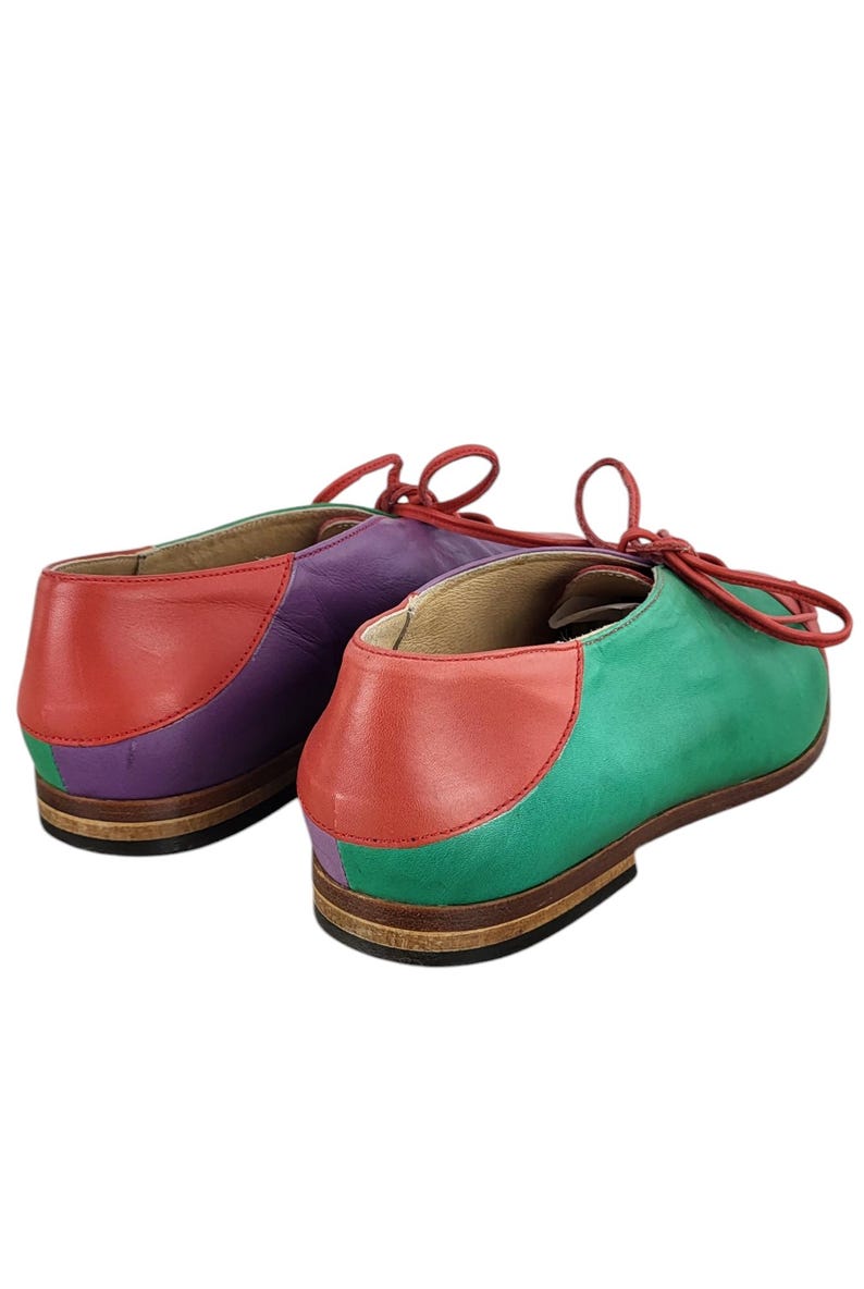 以下が含まれることがあります： 赤、紫、緑のパネルが付いたカラフルな革靴のペア。靴には靴ひもが付いており、茶色の靴底があります。