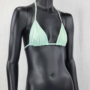 May include: A mint green bikini set displayed on a black mannequin. The two-piece swimsuit features a triangle top with halter straps and matching low-rise bottoms. The fabric has a slight sheen.