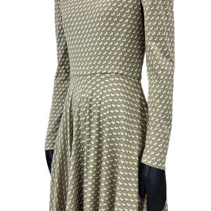 May include: A long-sleeved dress with a high neckline, featuring a repeating white horse pattern on a muted green background. The dress has a fitted bodice and a flared skirt, creating a classic silhouette.