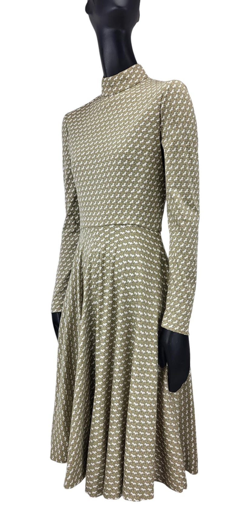 May include: A long-sleeved dress with a high neckline, featuring a repeating white horse pattern on a muted green background. The dress has a fitted bodice and a flared skirt, creating a classic silhouette.