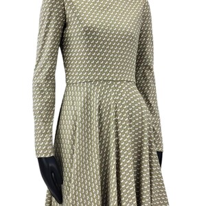 May include: A long-sleeved dress with a high neckline, displayed on a mannequin. The dress features a repeating white pattern on a muted green background. The skirt flares out from the waist.