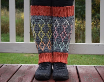 May include: A pair of gray crochet leg warmers with a colorful geometric pattern. The leg warmers have a red crocheted cuff at the top and bottom.