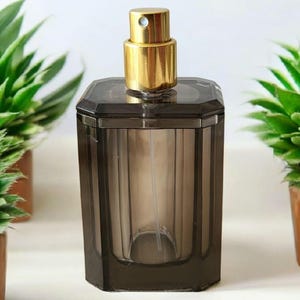 Peut inclure: Un flacon en verre transparent avec une teinte brun foncé et un embout pulvérisateur doré. Le flacon a une forme carrée avec des bords biseautés.