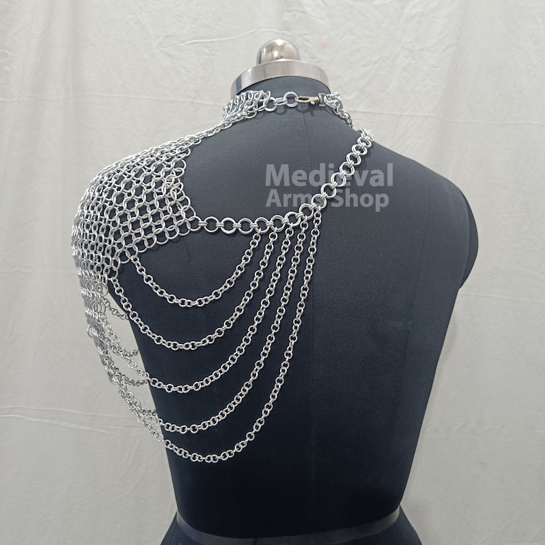 May include: Silver chainmail shoulder armor with a chainmail necklace. The armor is on a black mannequin. The text "Medieval Arm Shop" is visible on the image.