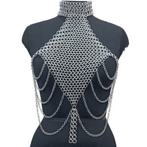 May include: A silver chainmail necklace with a choker style top and long chains hanging down the front. The necklace is displayed on a black mannequin.