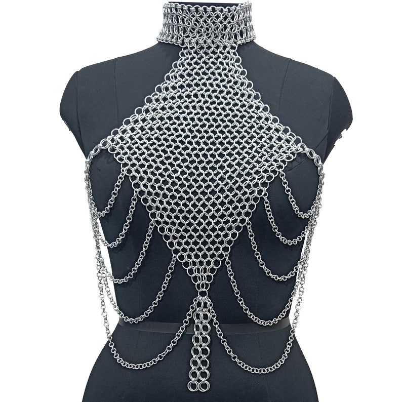 May include: A silver chainmail necklace with a choker style top and long chains hanging down the front. The necklace is displayed on a black mannequin.