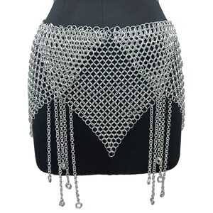 May include: A silver chainmail skirt with a triangular shape and dangling chains. The skirt is made of small, interconnected metal rings.