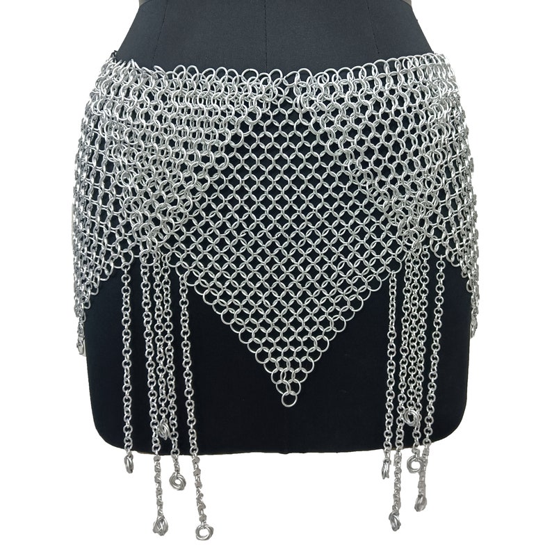 May include: A silver chainmail skirt with a triangular shape and dangling chains. The skirt is made of small, interconnected metal rings.