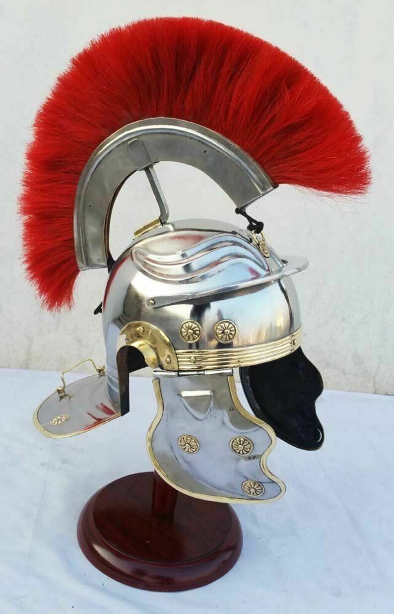 May include: A silver Roman helmet with a red horsehair crest, gold accents, and a black leather liner. The helmet is on a wooden stand.