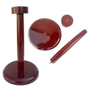May include: A wooden display stand for a hat or helmet. The stand is made of dark red wood and has a round base and a tall, cylindrical post. The post has a round top that is designed to hold a hat or helmet.