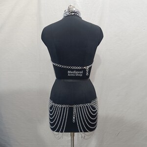 May include: Silver chainmail top and skirt set. The top is a halter style with a chainmail design. The skirt is a full skirt with a chainmail design. The set is on a black mannequin. The text "Medieval Arms Shop" is printed on the mannequin.