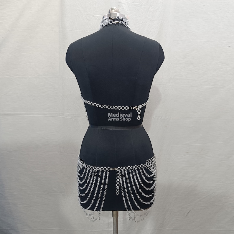 May include: Silver chainmail top and skirt set. The top is a halter style with a chainmail design. The skirt is a full skirt with a chainmail design. The set is on a black mannequin. The text "Medieval Arms Shop" is printed on the mannequin.