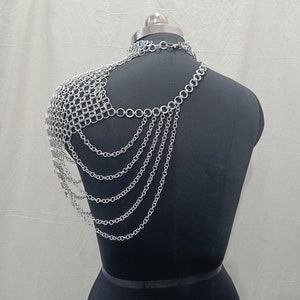 May include: Silver chainmail shoulder piece with multiple strands of chain hanging down the back. The chainmail is a delicate mesh pattern and the chains are linked together with small, round rings.