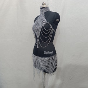May include: Silver chainmail top and skirt set. The top has a halter neckline and the skirt has a flowing hem. The set is made of interlocking metal rings.