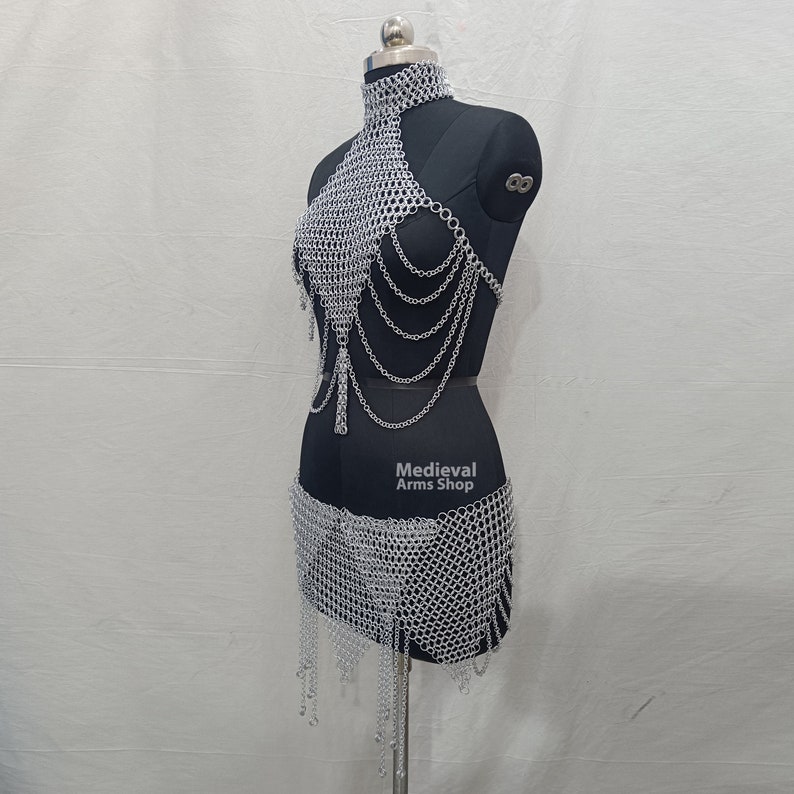May include: Silver chainmail top and skirt set. The top has a halter neckline and the skirt has a flowing hem. The set is made of interlocking metal rings.