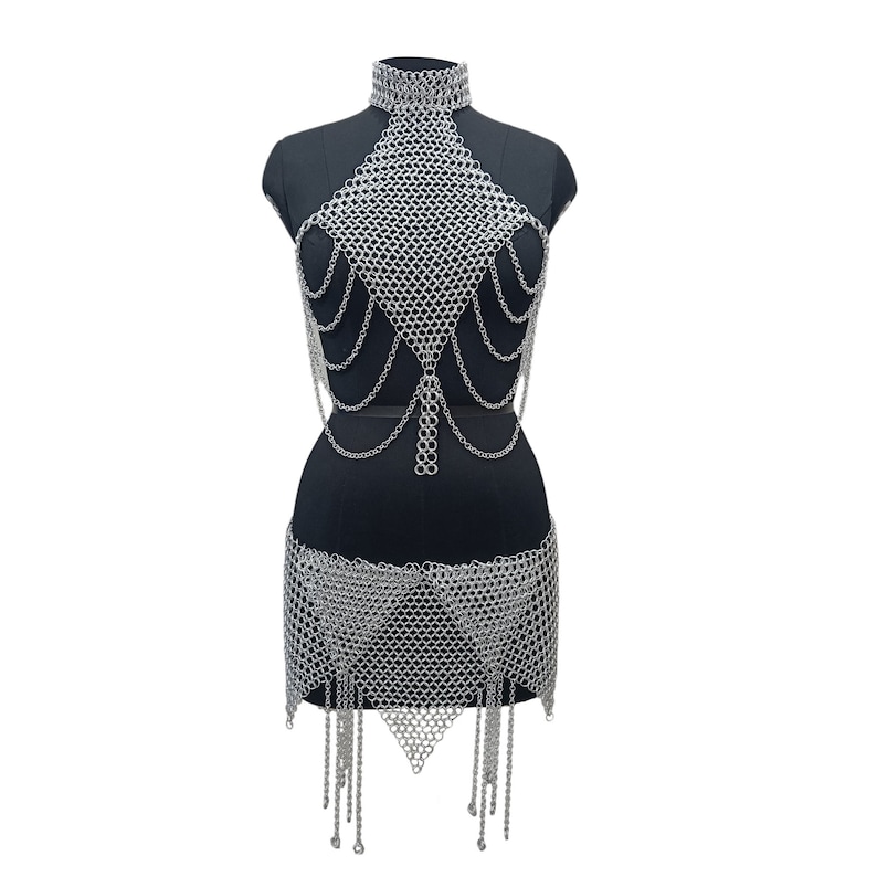 May include: A silver chainmail top and skirt set. The top has a halter neckline and a triangular shape. The skirt is a mini skirt with a triangular panel in the front and a fringe hem.