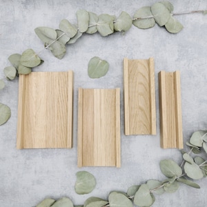 Könnte beinhalten: Vier rechteckige Holzhalter in verschiedenen Größen, aus hellem Holz gefertigt. Die Halter haben ein gerilltes Design und sind auf einer grauen Oberfläche angeordnet, mit Eukalyptusblättern verstreut.