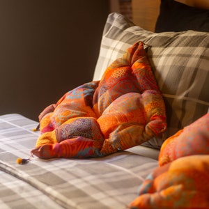 May include: A bed with a patterned pillow in shades of orange, red, and blue. The pillow is on top of a gray and white plaid pillow.