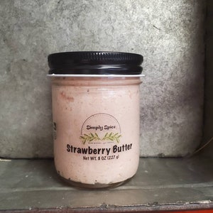 May include: A glass jar with a black lid filled with pink strawberry butter. The label reads "Simply Spice" and "Strawberry Butter" with a net weight of 8 oz (227 g).