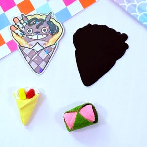 May include: A set of four colorful food-themed stickers. The stickers feature a cartoon character in a crepe, a crepe with fruit and whipped cream, a crepe with a green leaf, and a black and white silhouette of a crepe.