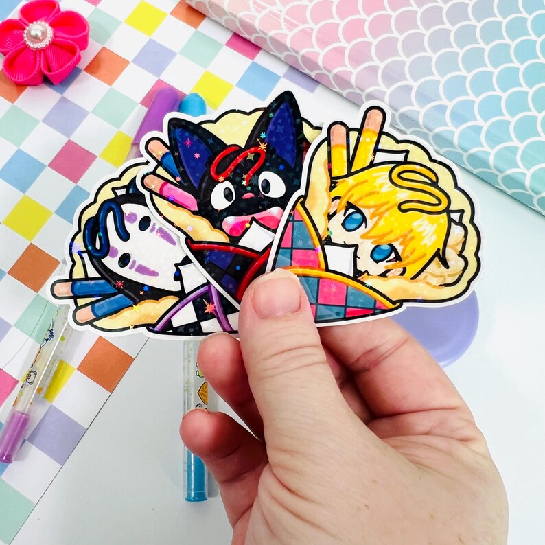 Pu&ograve; includere: Tre adesivi di personaggi dei cartoni animati colorati con No Face, Jiji e un personaggio biondo con un'aureola. Gli adesivi sono su uno sfondo bianco e sono circondati da un bordo bianco.