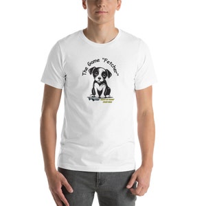 May include: White t-shirt featuring a black and white cartoon dog illustration. The text "The Game "Fetcher"" is printed on the shirt.