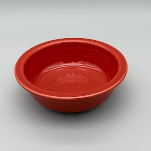 May include: A vibrant red ceramic bowl with a circular design in the center. The bowl has a wide rim and a smooth, glossy finish. The bowl is a solid, bright red color.