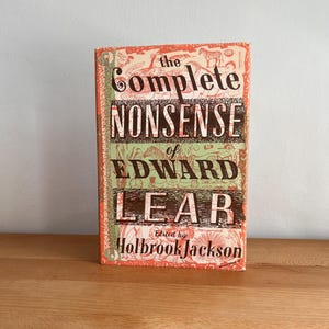 May include: A hardcover book titled The Complete Nonsense of Edward Lear, edited by Holbrook Jackson. The cover features a vibrant orange and green background with intricate black line drawings of various animals and figures throughout the design.