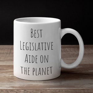 May include: White ceramic coffee mug with black text that reads "Best Legislative Aide on the Planet".