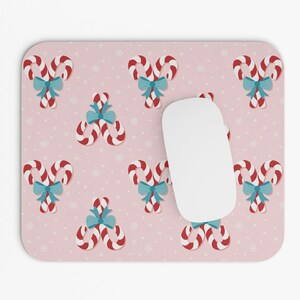 May include: Pink mouse pad with a repeating pattern of candy canes with blue bows. A white computer mouse is on the mouse pad.