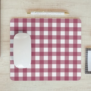 May include: A white computer mouse sits on a pink and white gingham desk mat. The mat is on a light wood surface.